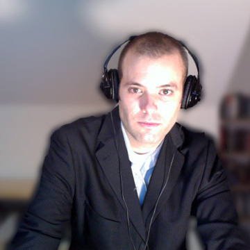 Andy wearing a suit and headphones, working at his desk